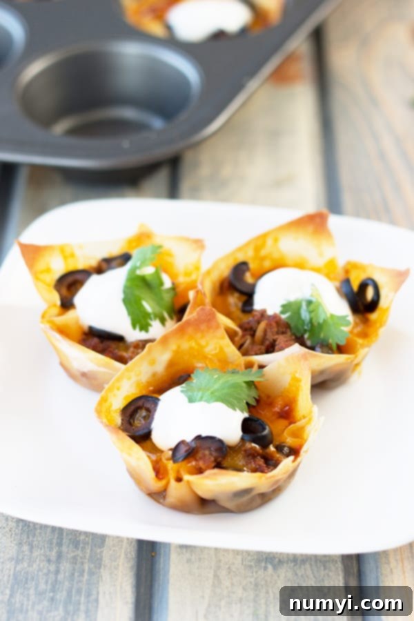 Three enchilada cups on a white plate topped with a dollop of sour cream and olives, ready to be served