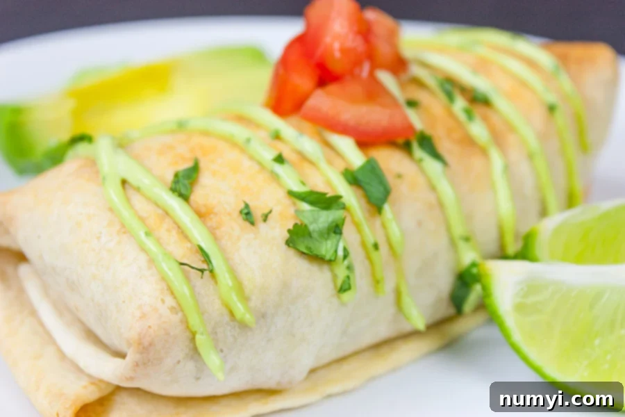 Baked Chicken Chimichangas garnished with cilantro, tomato, and lime wedges on a white plate.