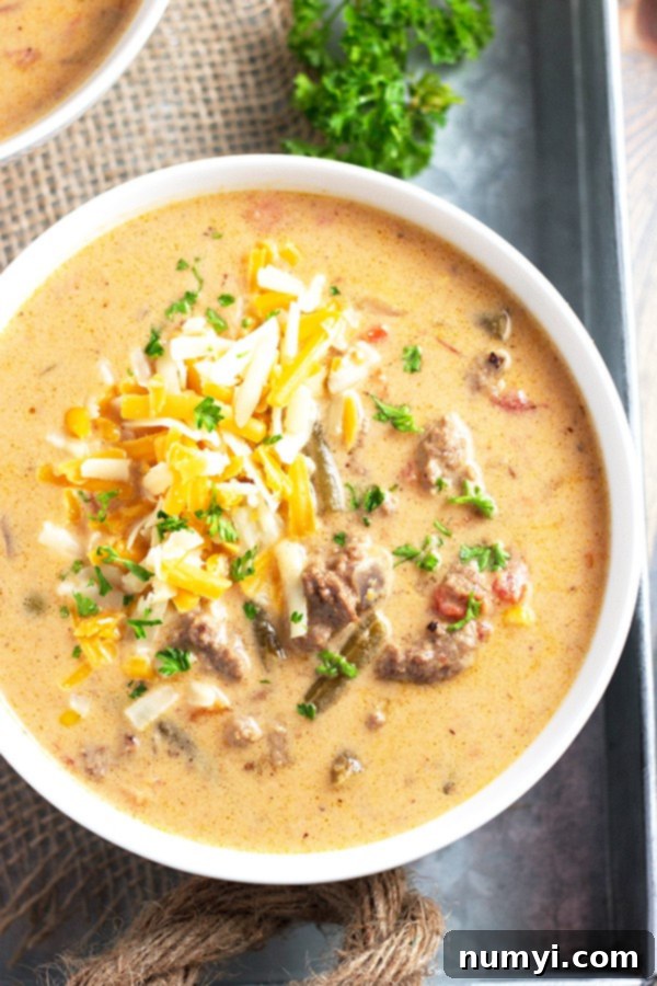 cheeseburger soup made in the slow cooker and served in a large white bowl topped with cheese and green herbs for garnish