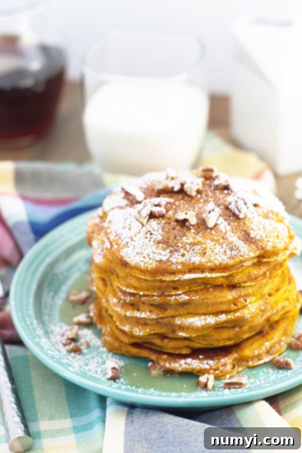 Ultimate Pumpkin Spice Pancakes 3 A towering stack of fluffy pumpkin pancakes, generously adorned with powdered sugar, a sprinkle of chopped nuts, and a luscious drizzle of golden maple syrup.