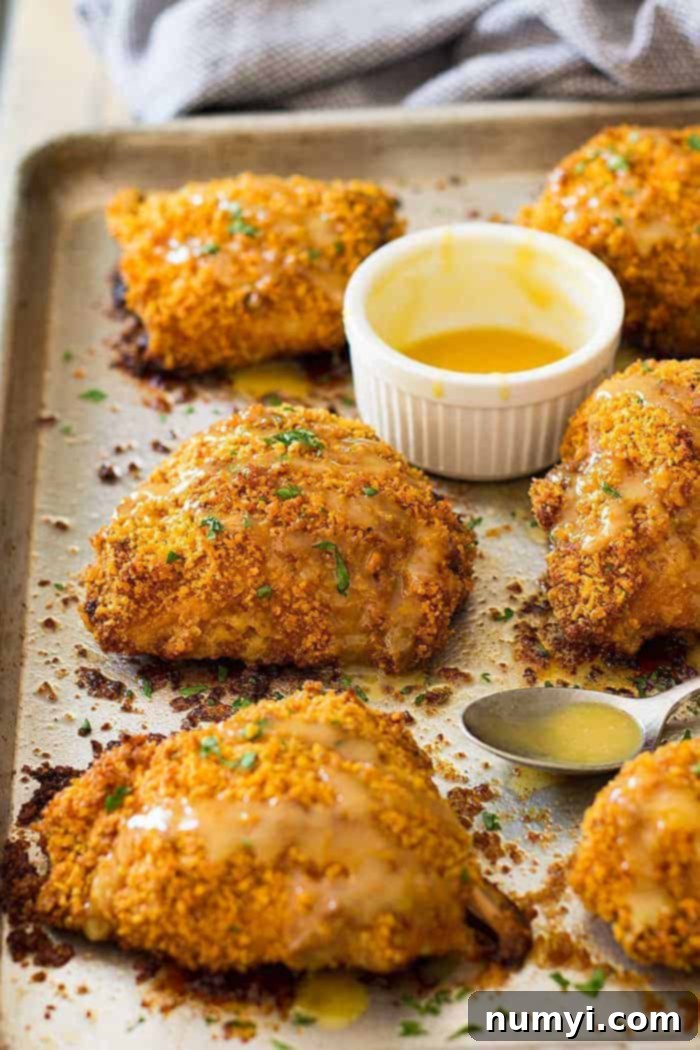 Crispy oven fried chicken thighs on a baking sheet, served with a side of honey mustard dipping sauce.