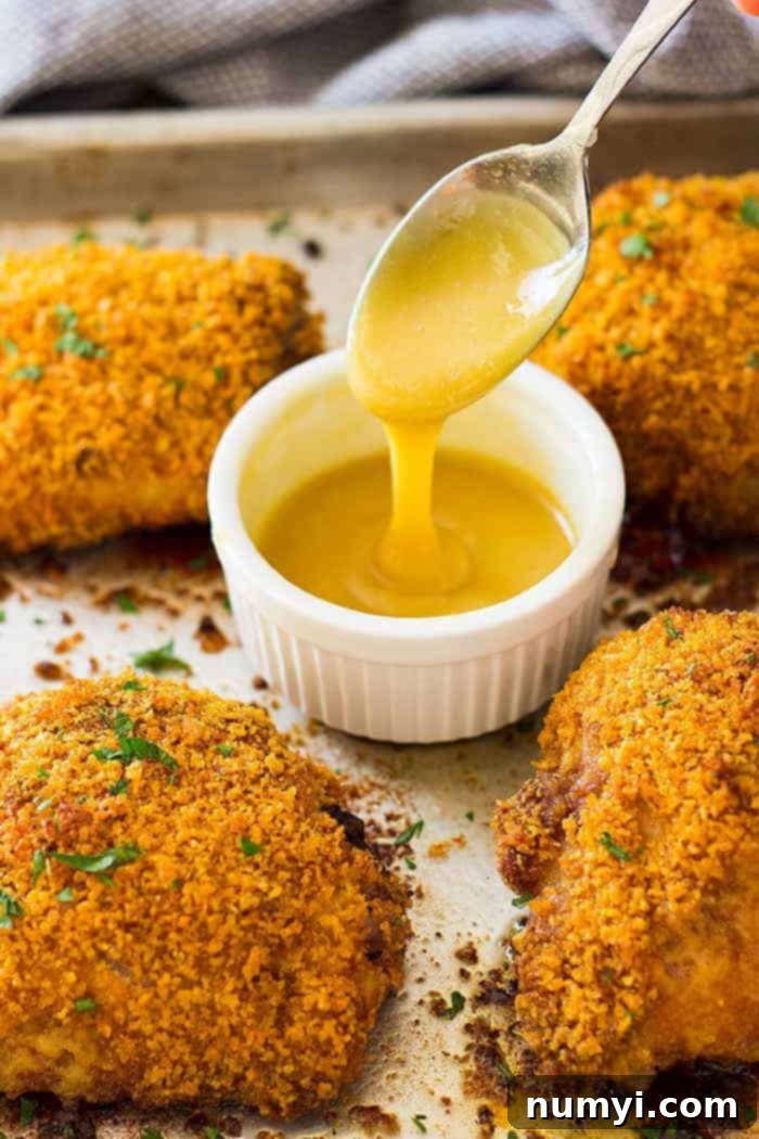 Golden-brown crispy oven baked chicken thighs on a sheet pan, with a small bowl of creamy homemade honey mustard sauce beside it.