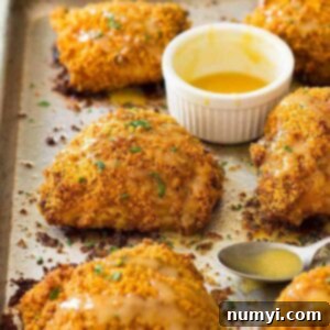 Delicious crispy oven baked chicken thighs presented on a sheet pan, accompanied by a small bowl of honey mustard sauce.