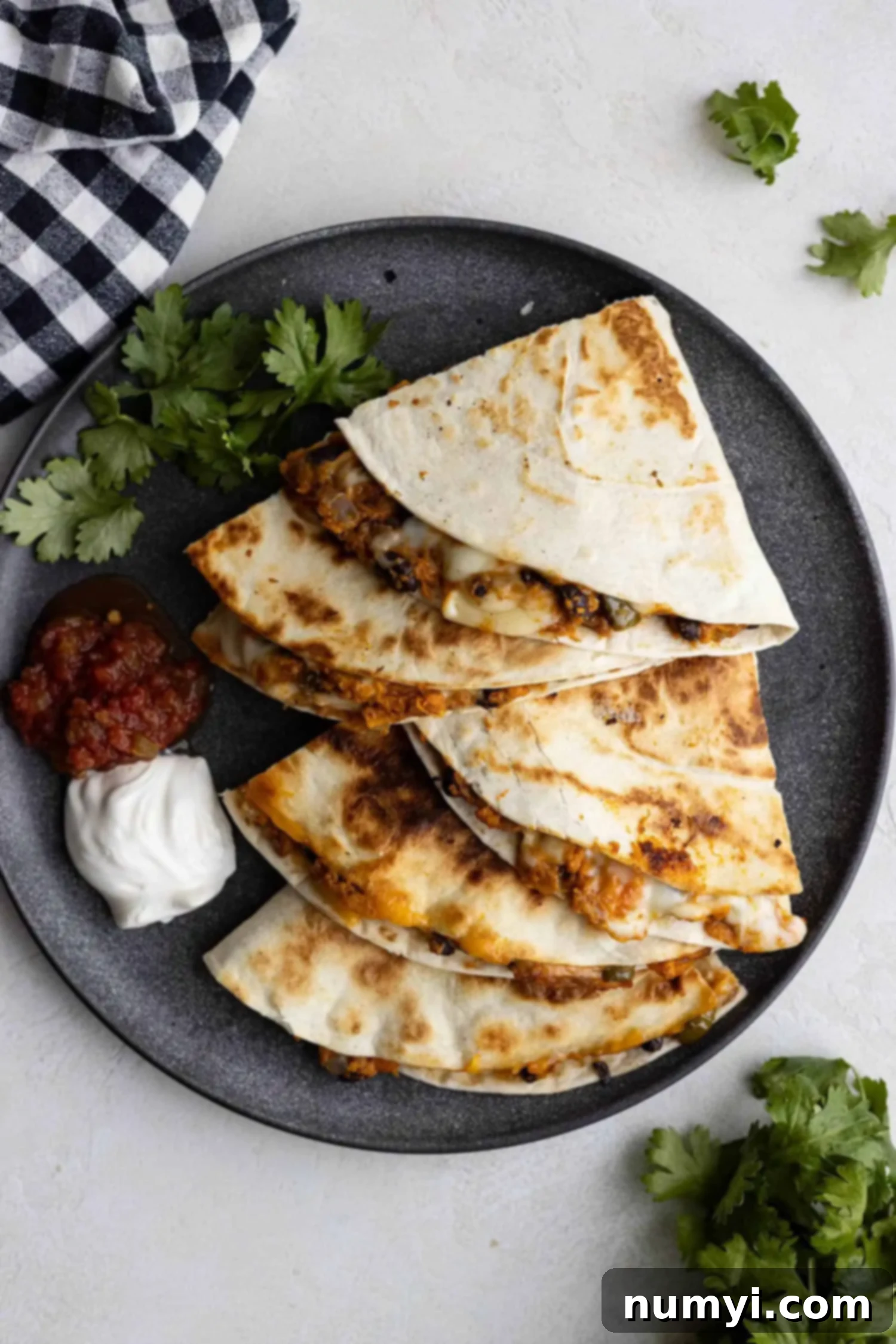 Overhead view of crispy black bean sweet potato quesadillas on a dark plate, perfectly cut in half, with a dollop of sour cream and fresh salsa on the side, ready to be enjoyed.