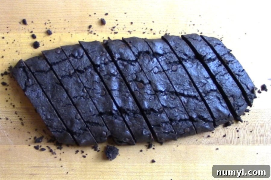 Freshly sliced chocolate biscotti arranged diagonally on a wooden cutting board, ready for their second bake.