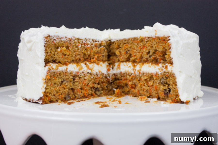 Homemade carrot cake on white cake platter cut to show texture, ready to be served.