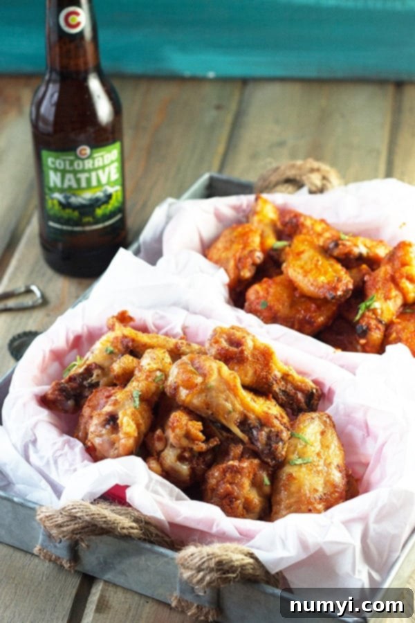 Two baskets of crispy baked garlic sriracha chicken wings, one with a fiery dry rub and the other glistening with a rich, saucy glaze. A bottle of beer is visible in the background, setting the scene for a perfect game day treat.