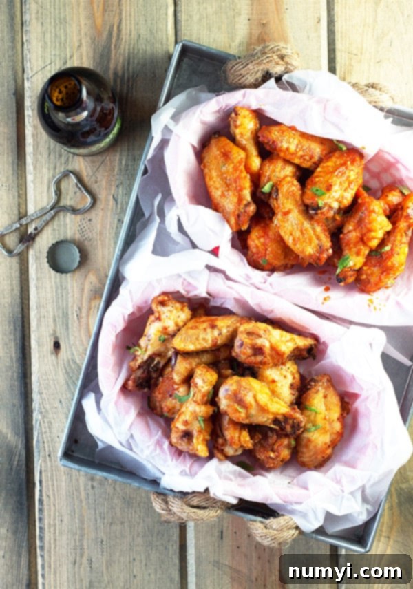 A side-by-side view of two baskets of perfectly baked sriracha chicken wings, one showcasing the crispy dry rub and the other the glistening, saucy coating, ready to be enjoyed.