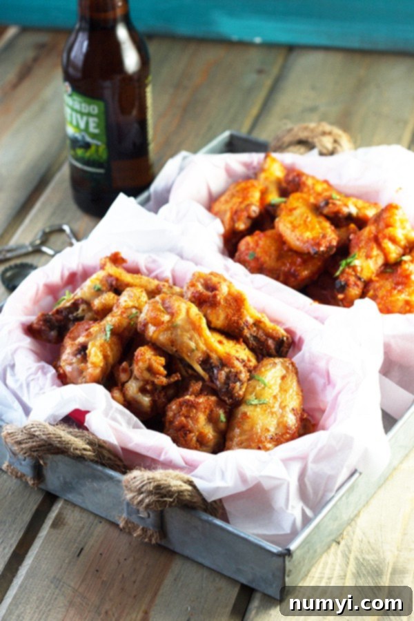 Crispy dry rub chicken wings in the foreground, with a refreshing bottle of beer and a basket of saucy sriracha wings in the background, illustrating a complete game day spread.