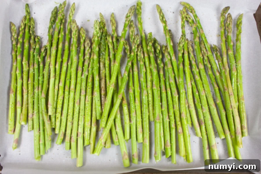 Raw asparagus spears neatly arranged on a parchment-lined baking sheet, ready for roasting.