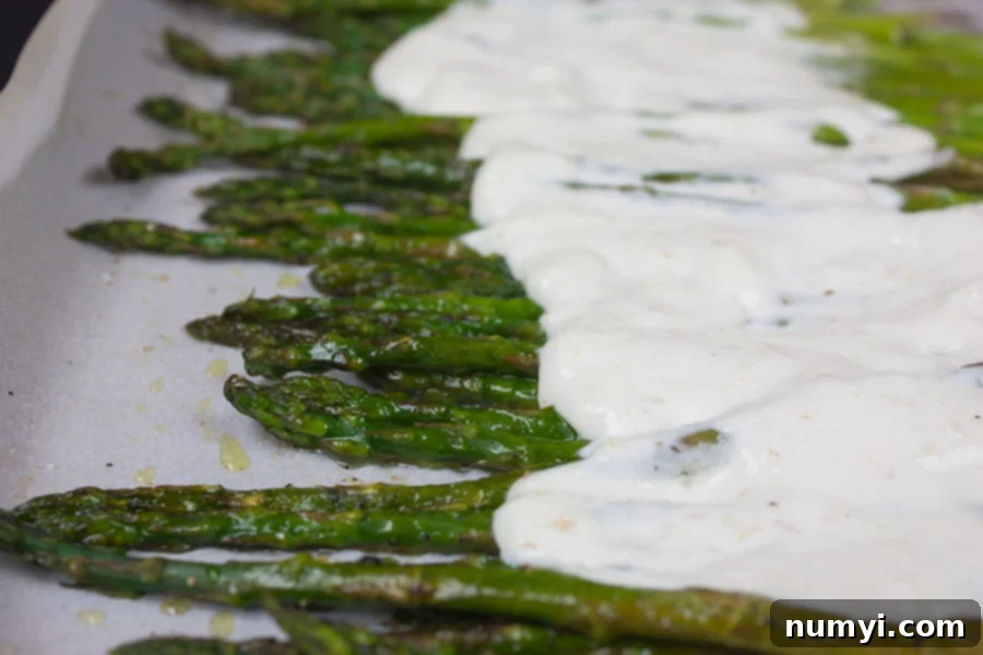 Asparagus with a horseradish cream sauce on a baking sheet pan.