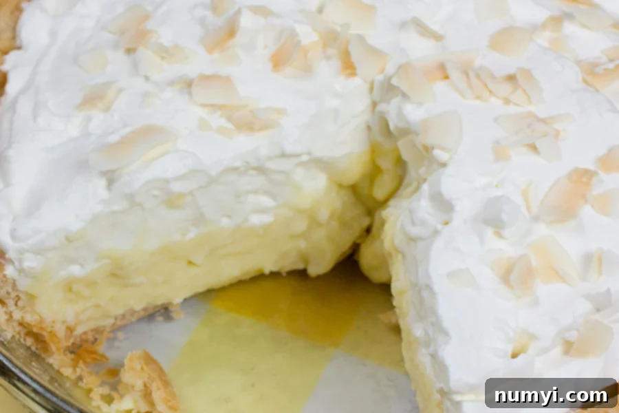 Coconut Cream Pie with a slice removed, showing the layers of crust, custard, and whipped cream.