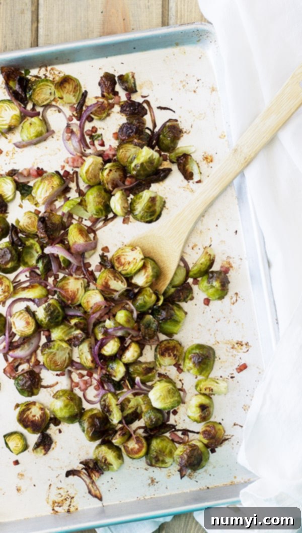 Oven-Roasted Brussels Sprouts with Ham & Caramelized Onions 2 A sheet pan generously loaded with golden-brown roasted Brussels sprouts, savory ham pieces, and thinly sliced caramelized onions, ready to be served.