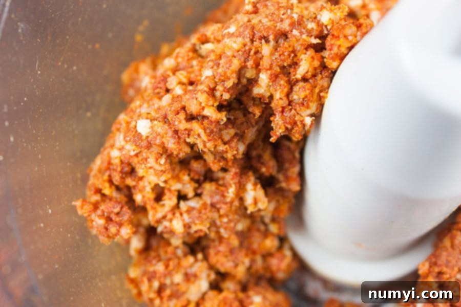 Close-up of raw bacon paste being processed in a food processor bowl, showing the finely blended mixture of bacon and spices, ready to coat the chicken.