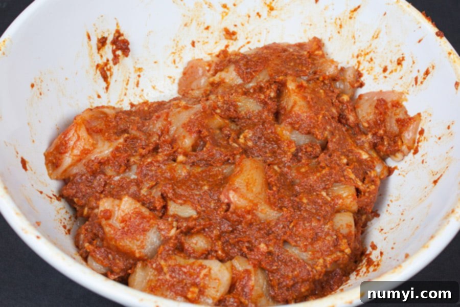 Chicken pieces thoroughly covered in the rich bacon paste and barbecue sauce marinade, resting in a white mixing bowl, ready for marination.