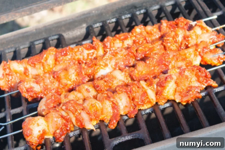 Bacon Paste BBQ Chicken Kebabs sizzling on a hot outdoor grill, smoke rising, with visible grill marks developing on the chicken.