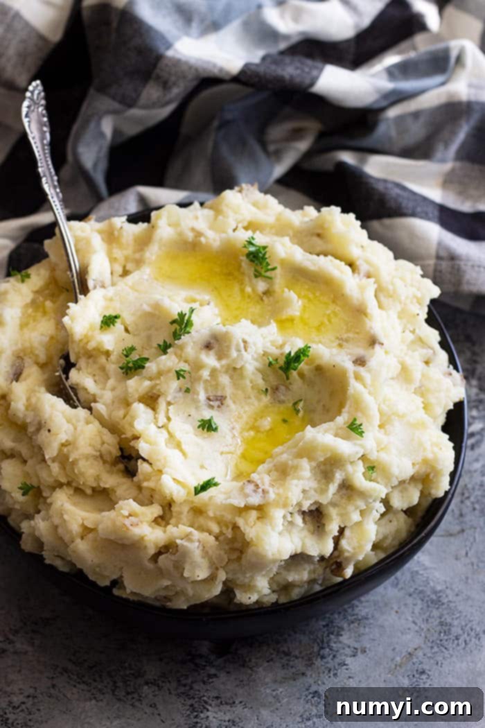 Large bowl of slow cooker mashed potatoes topped with butter and chopped parsley to garnish.