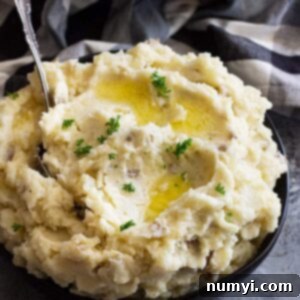 Large bowl of slow cooker mashed potatoes topped with butter and chopped parsley to garnish.