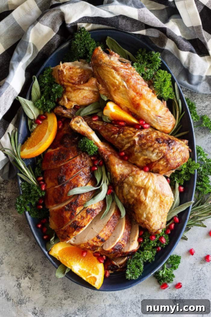 An overhead shot of a golden-brown Beer and Butter Turkey resting on a serving platter, beautifully decorated with fresh orange slices, aromatic herbs, and ruby-red pomegranate arils, ready to be carved.