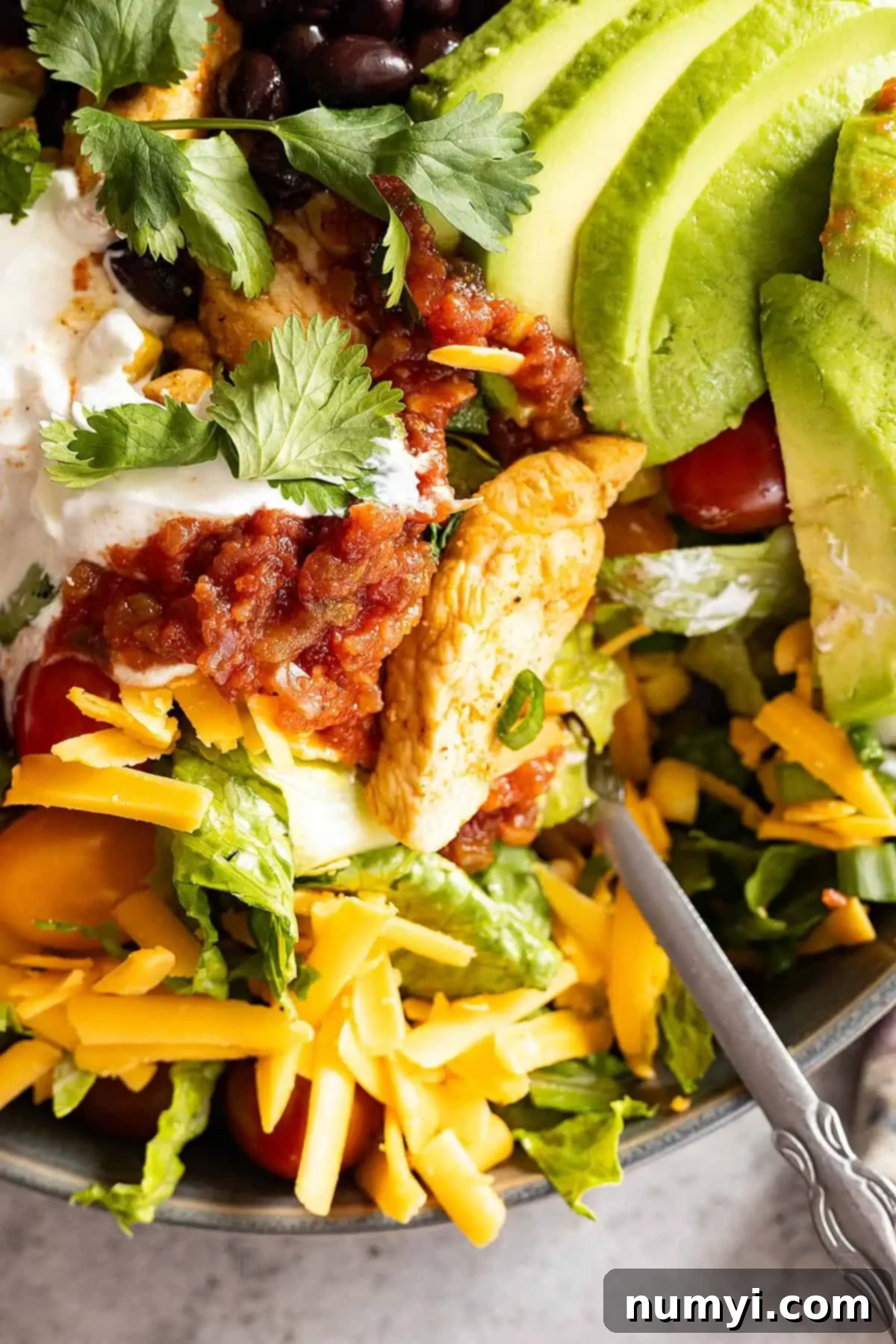 Fiesta Chicken Bowls 6 Close-up view of a vibrant chicken taco bowl with a fork nestled in the salad, ready to be eaten. Highlights the freshness and texture of the ingredients.
