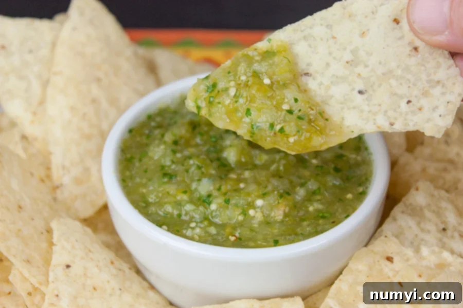 A tortilla chip is dipped into a bowl of vibrant green homemade roasted tomatillo salsa verde, highlighting its perfect texture and fresh appeal.
