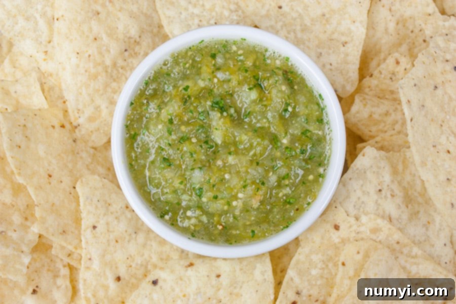 Homemade roasted tomatillo salsa verde served in a small white ramekin, surrounded by crunchy tortilla chips, ready for dipping.