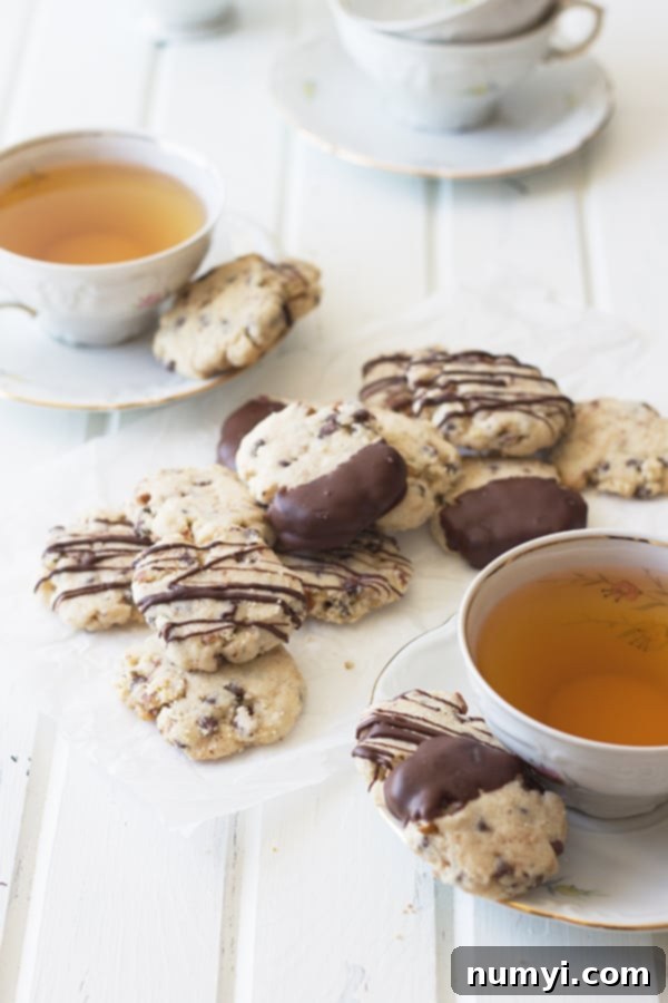 A charming display of golden-brown chocolate chip pecan shortbread cookies beside two steaming cups of tea, inviting you to indulge in a perfect pairing.