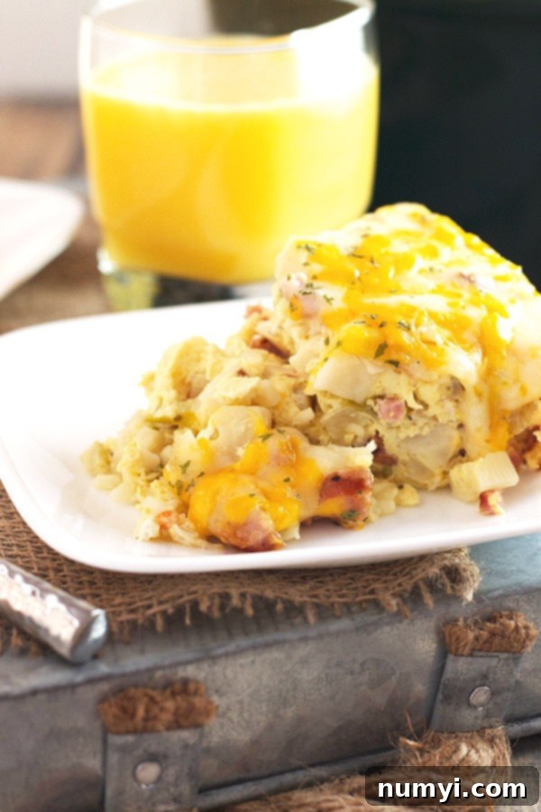 Overnight Slow Cooker Sausage and Potato Bake 3 A generous, cheesy serving of slow cooker breakfast casserole on a white plate, positioned in front of a glass of refreshing orange juice, illustrating a perfect breakfast pairing.