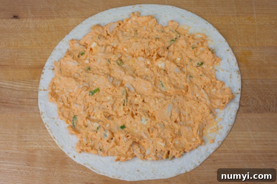 Buffalo chicken mixture spread over a flour tortilla on a cutting board.