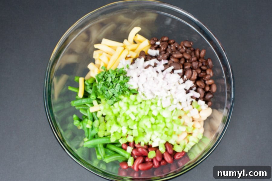 Five Bean Salad ingredients in a glass mixing bowl, including various beans, celery, shallots, and parsley.