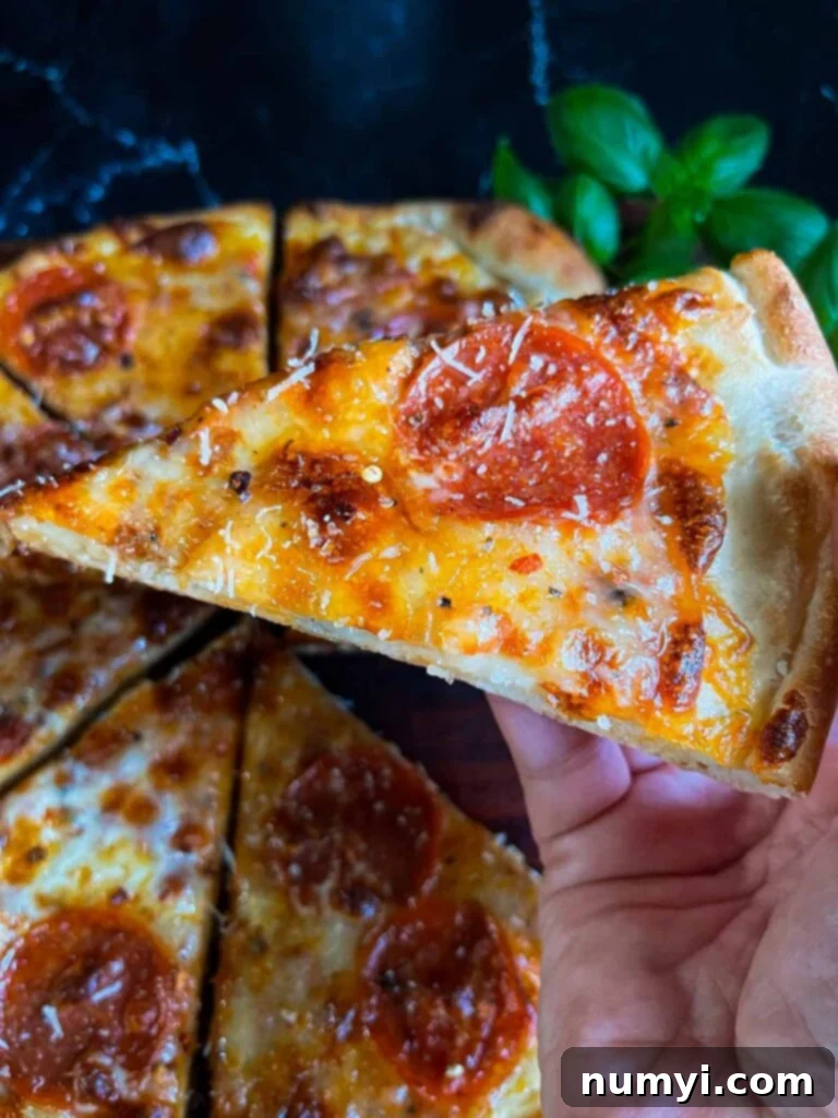 A hand holding up a slice of homemade pepperoni pizza, showing the sturdy, delicious crust.