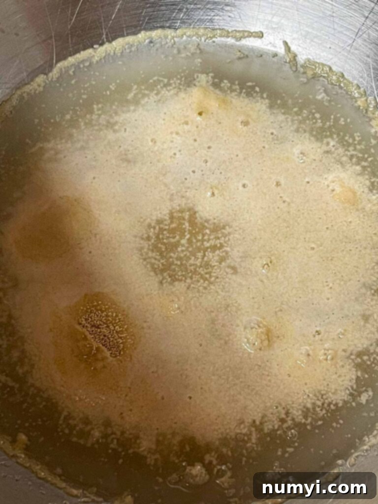 Active dry yeast blooming in a stand mixer bowl with warm water and sugar.