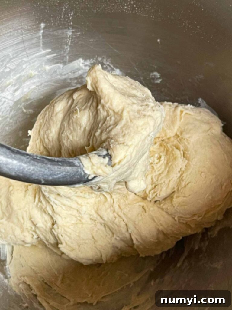 Pizza dough being mixed with a dough hook in a stand mixer bowl.