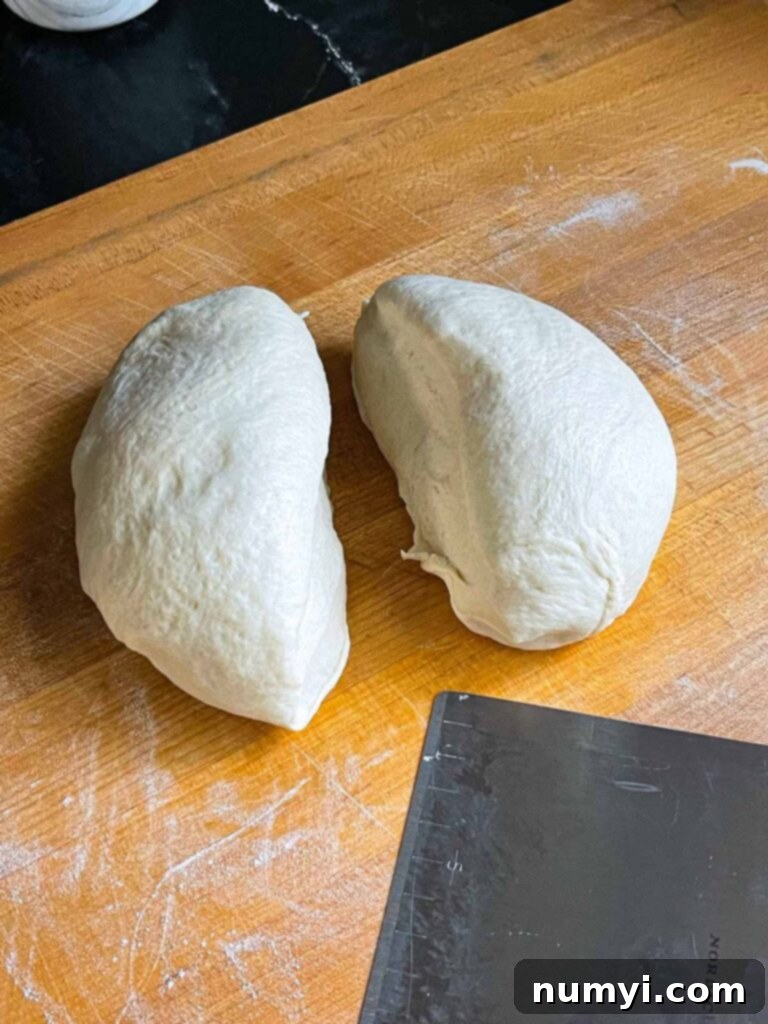 Pizza dough divided into two portions on a large wooden cutting board after its first rise.