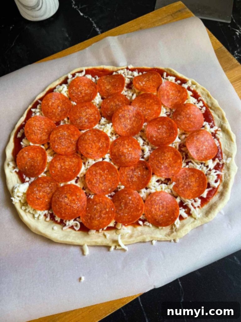An unbaked pepperoni pizza on parchment paper, ready to be cooked.