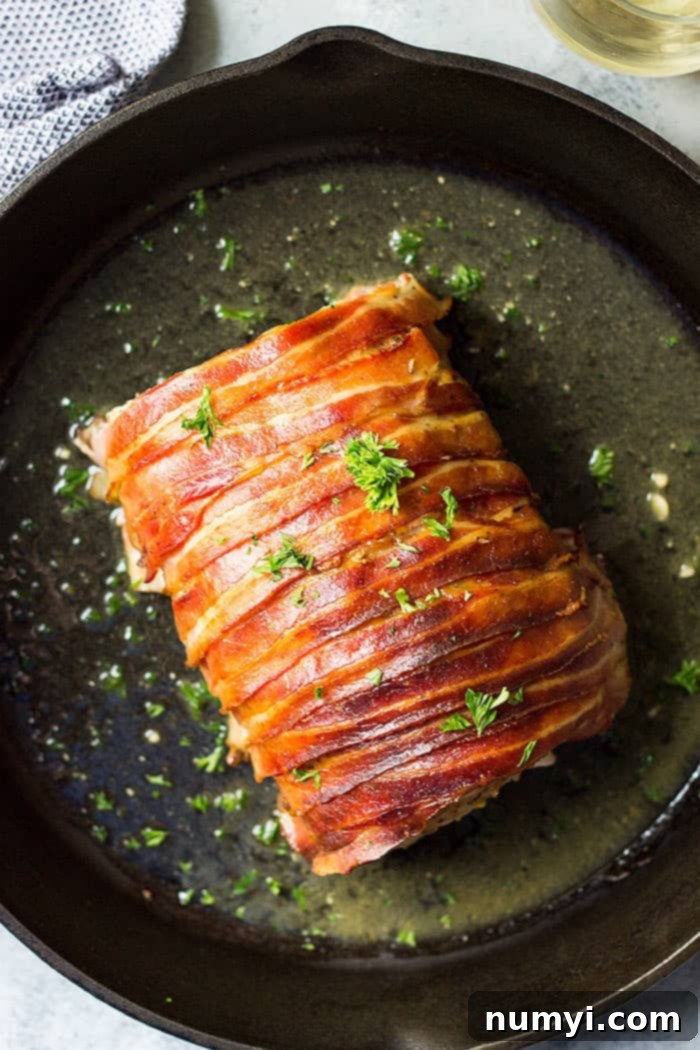 Crisp Bacon-Wrapped Pork Loin 2 A perfectly cooked pork loin wrapped in crispy bacon, resting in a cast iron skillet, ready to be sliced and served.