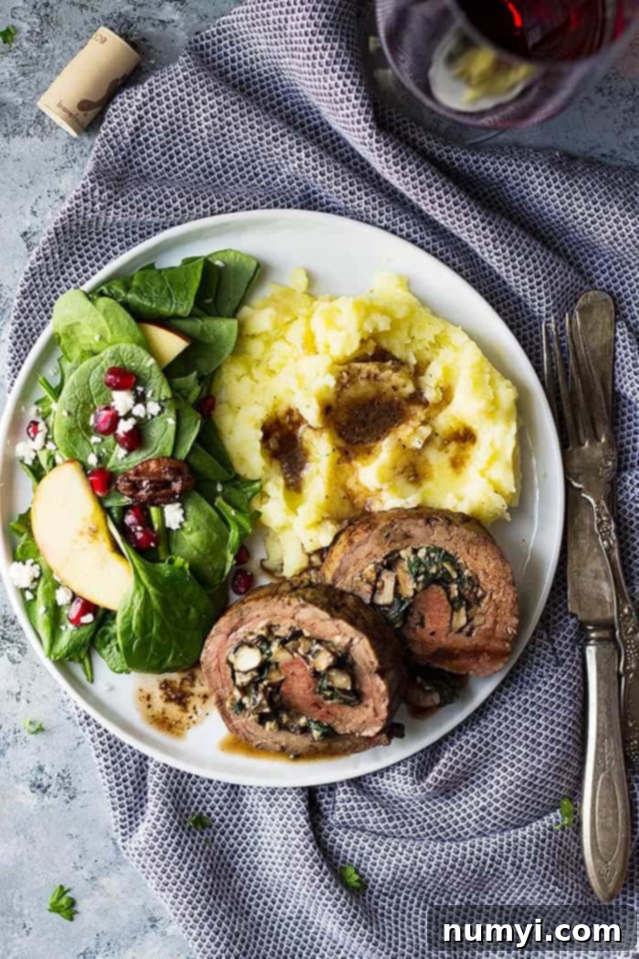 A plate filled with sliced mushroom and blue cheese stuffed flank steak, mashed potatoes, and salad. 
