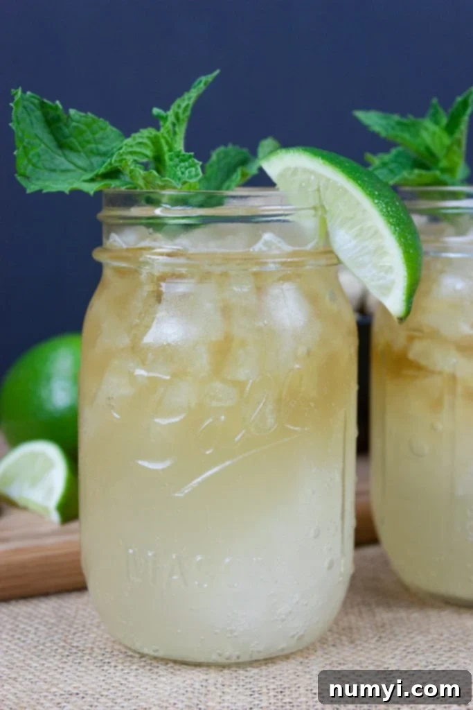 A vibrant Kentucky Mule served in a large mason jar, beautifully garnished with fresh mint leaves and a bright lime wedge. The drink is filled with ice, signaling its refreshing coolness.