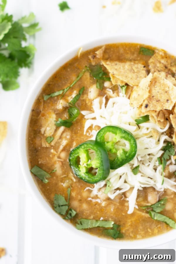 Slow Cooker White Chicken Chili 4 A close-up overhead view of Slow Cooker White Chicken Chili in a white bowl, generously topped with chopped fresh jalapeños and grated Parmesan cheese, highlighting the rich texture of the chili.