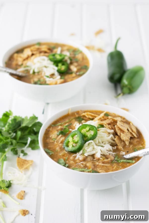 Slow Cooker White Chicken Chili 5 Two bowls of white chicken chili, garnished with shredded cheese and fresh jalapeño slices, ready to be served.