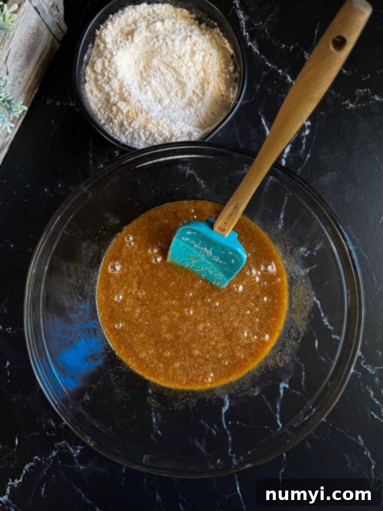 Mixing the wet and dry ingredients for salted butterscotch pretzel cookie dough in a glass bowl on a dark surface.
