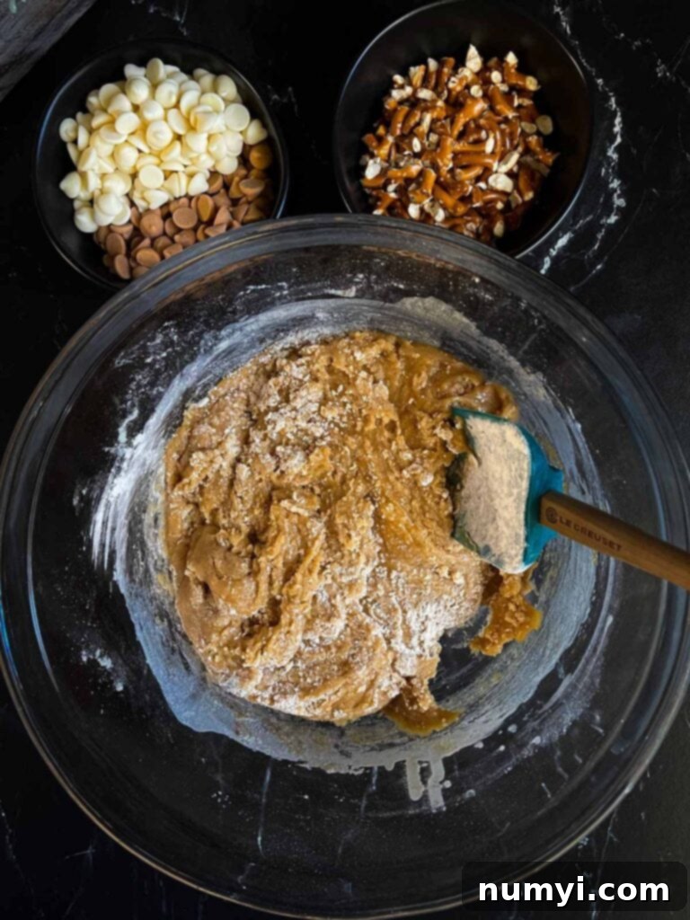 Salted butterscotch pretzel cookie dough in a glass bowl on a dark surface, showing the stage before adding chips and pretzels.