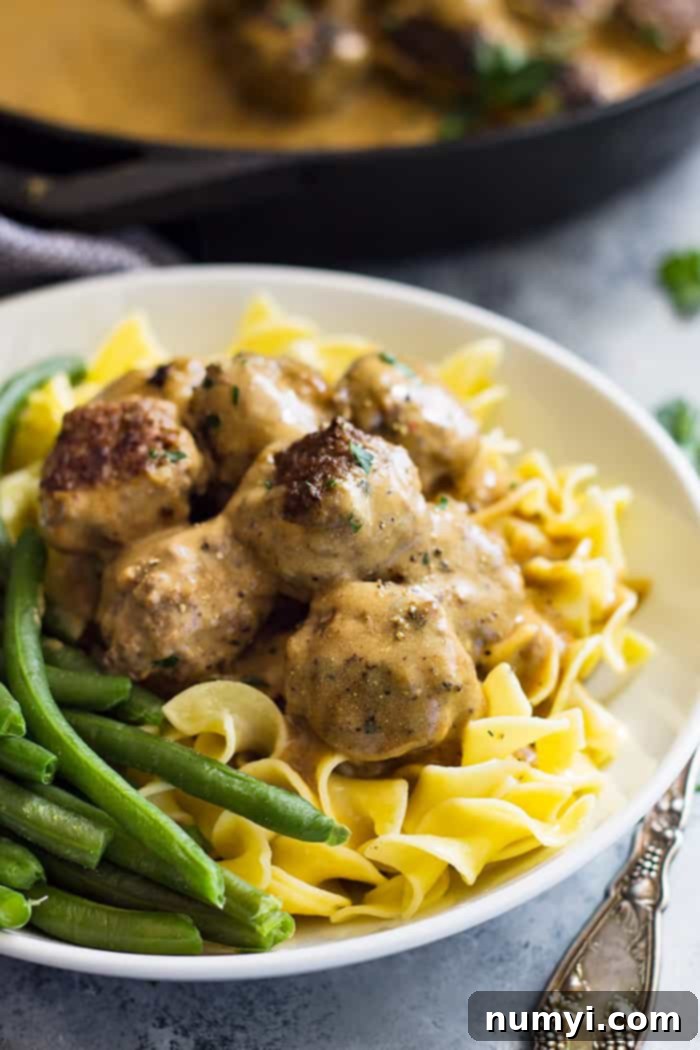 Swedish meatballs piled high on top of egg noodles with a side of green beans. 