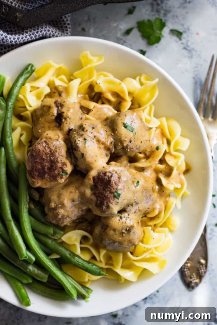 A big bowl of egg noodles topped with Swedish meatballs and a side of green beans. 