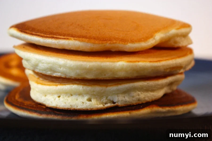 A tall, perfectly cooked stack of the best ever fluffy pancakes, drizzled with syrup and a pat of butter on top, ready to be enjoyed for a delicious breakfast.