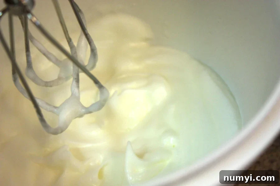 Perfectly whipped egg whites forming stiff peaks in a glass bowl, showcasing the crucial step for achieving fluffy pancakes.