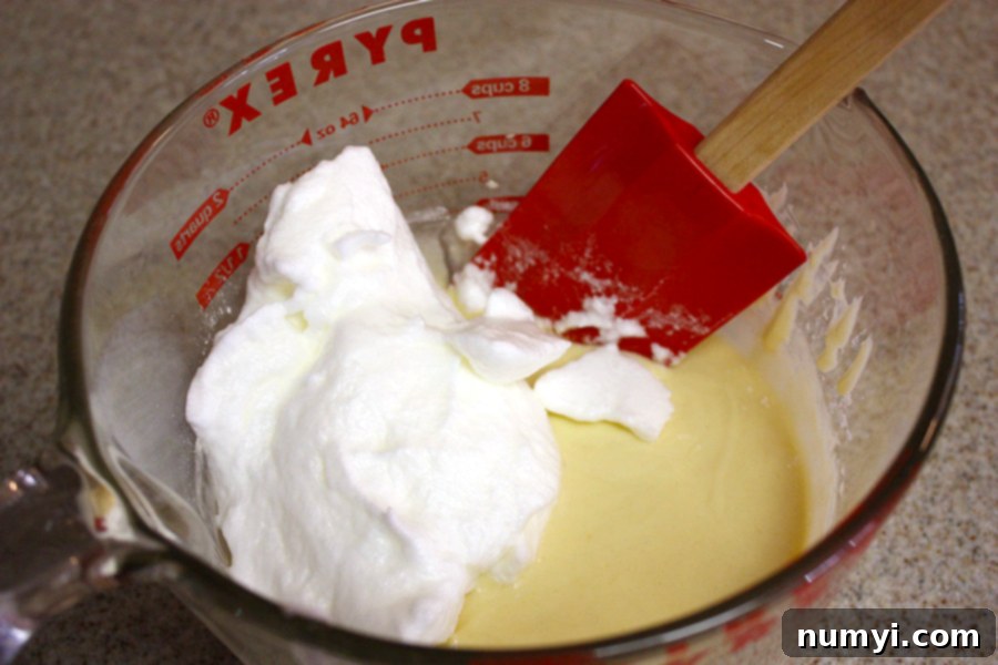 Pancake batter gently mixed with whipped egg whites, showcasing the light and airy consistency in a clear glass measuring bowl, ready for cooking.