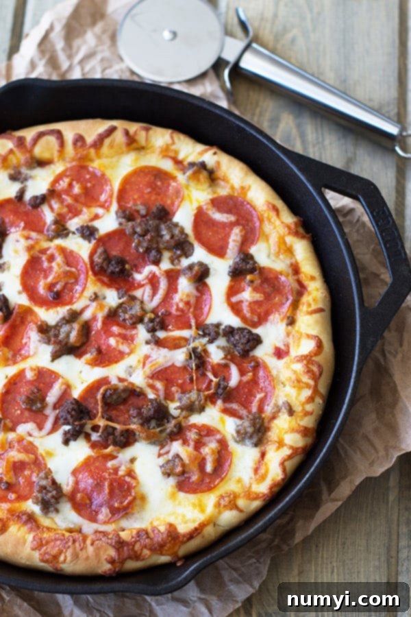 A cast iron skillet overflowing with a golden-brown deep dish pizza, generously topped with three kinds of meats and abundant melted cheese, ready to be served.