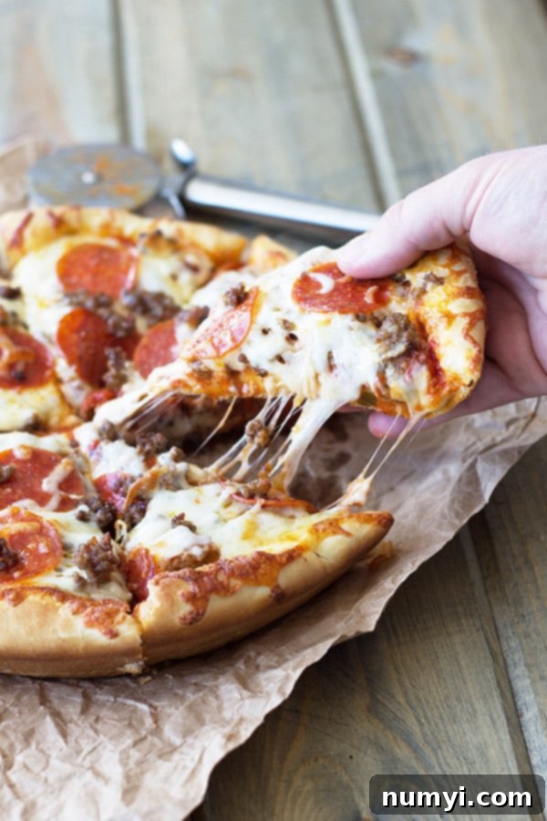 A hand pulling a slice of deep dish pizza from a cast iron skillet, with melted cheese stretching enticingly from the main pie to the lifted slice.