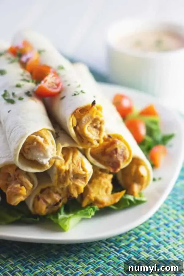 Close-up of baked chicken taquitos arranged on a white serving plate, garnished with fresh chopped tomatoes and cilantro, showcasing the golden-brown tortillas and delicious filling.